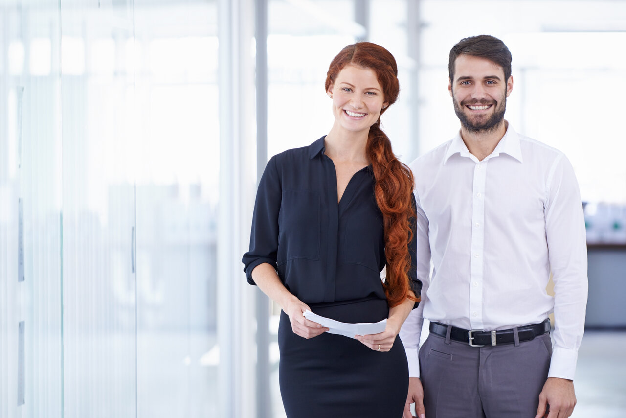 Zwei Menschen in smart-casual-business-Kleidung stehen vor einem neutralen Hintergrund