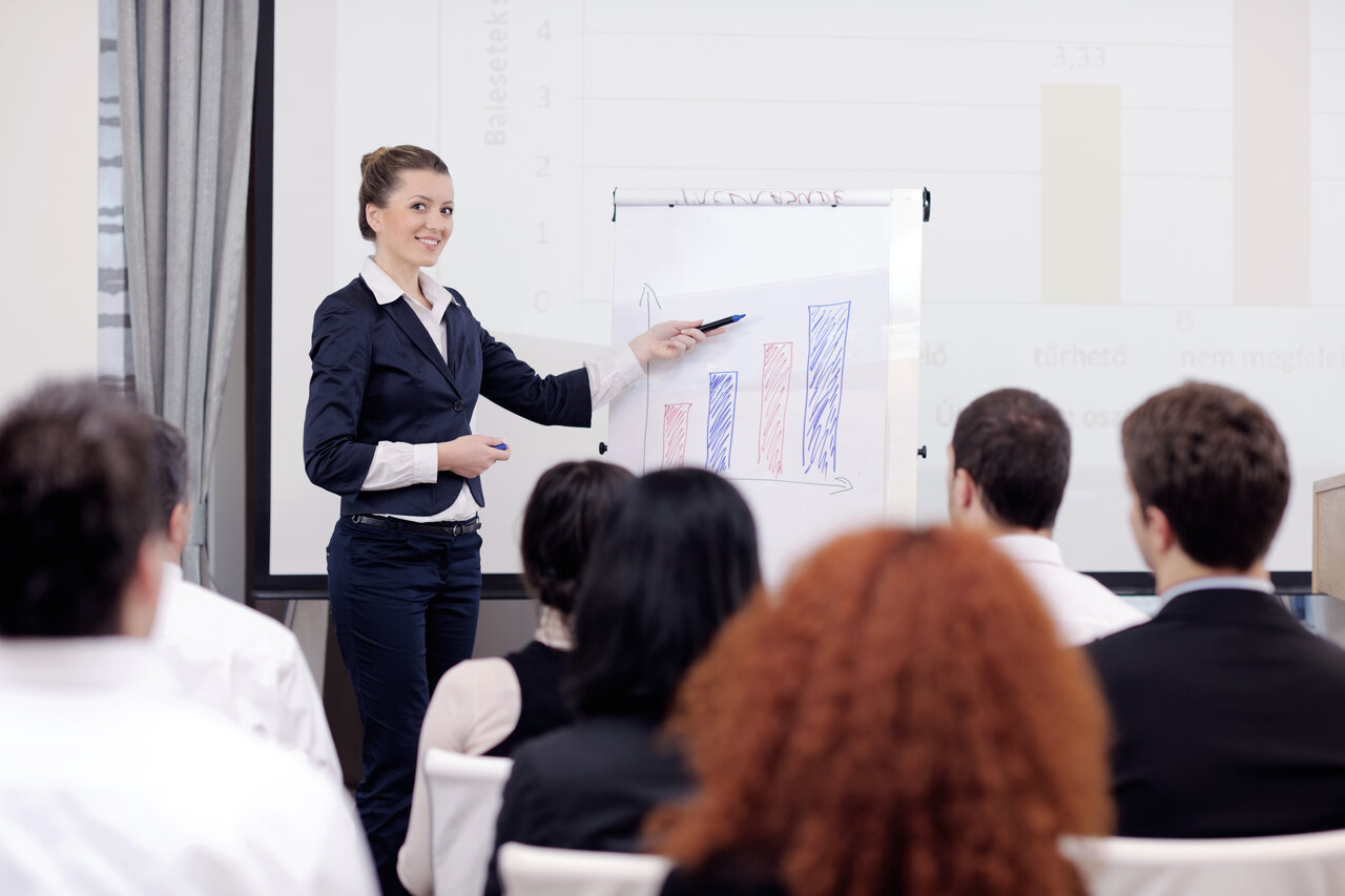 Eine Frau hält eine Präsentation vor sitzenden Menschen in einem Business-Kontext.