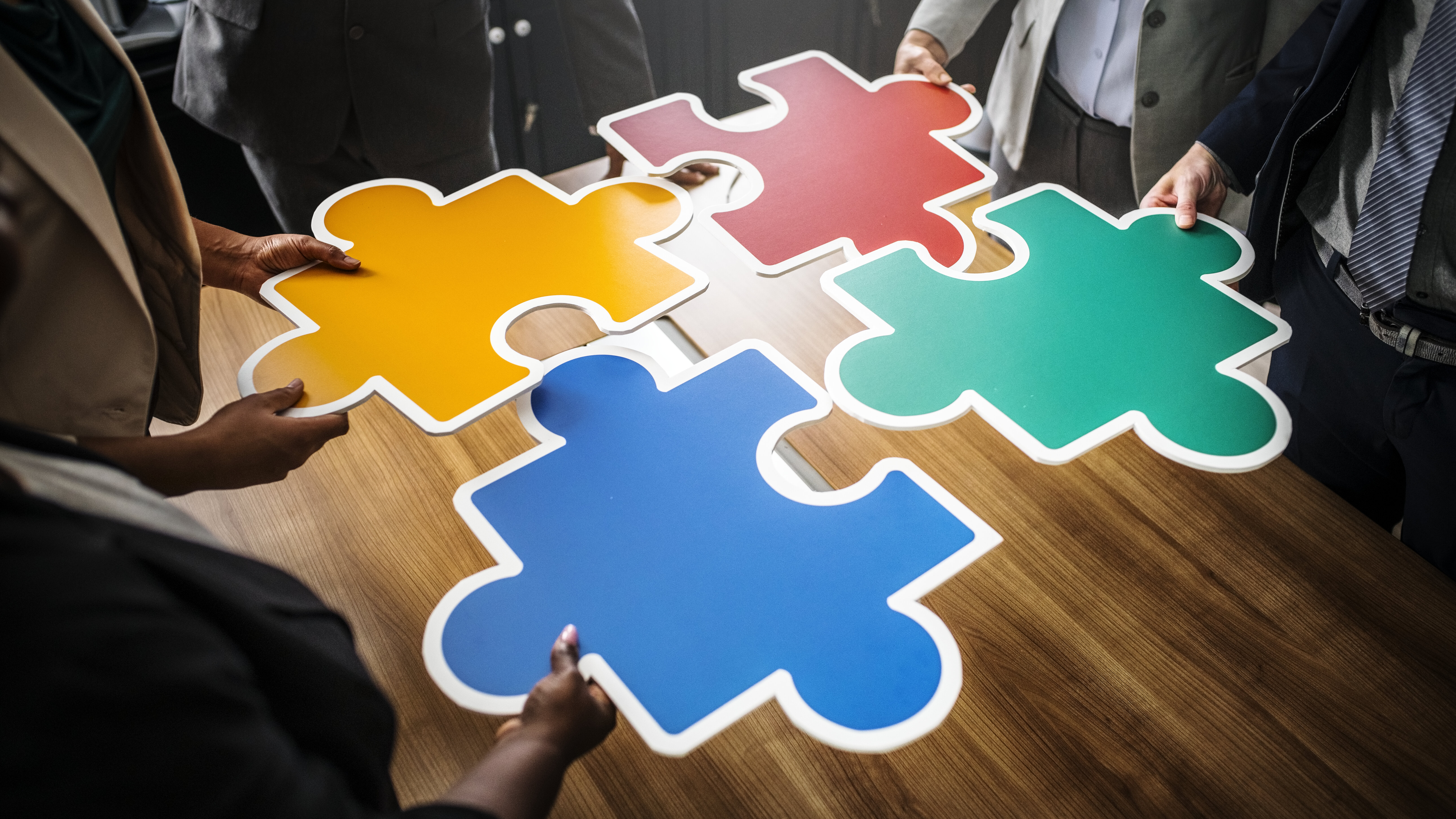 Menschen schieben vier verschiedenfarbige sehr große Puzzelteile zusammen